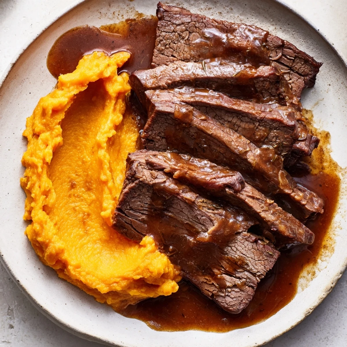 Classic brisket, sliced, alongside creamy mashed sweet potatoes, a tender, flavorful main course.