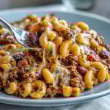 Creamy One-Pan High Protein Chili Mac topped with sour cream, green onions, and melted cheddar in a rustic bowl.