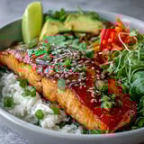 A colorful Soy Ginger Salmon Bowl garnished with green onions, sesame seeds, and lime wedges on a white plate.