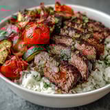 A close-up view shows juicy, perfectly cooked steak alongside caramelized cherry tomatoes and red onions, all arranged in a hearty sheet pan steak and veggie bowl ready for a weeknight dinner.
