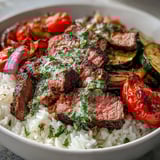 This Grilled Steak Bowl features juicy steak, roasted veggies, and a bright green drizzle of chimichurri sauce on a bed of rice.