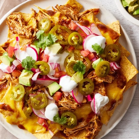 Golden-brown loaded nachos with pulled pork, a cheesy queso, and vibrant toppings, ready to enjoy.