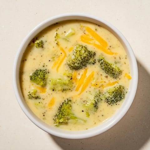 Close-up of a bubbling broccoli cheese soup, showcasing melted cheddar cheese and tender broccoli florets.