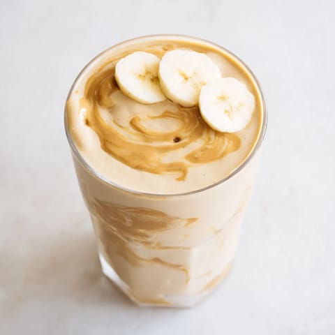 Freshly blended peanut butter banana smoothie, swirled with vanilla, served cold in a glass.