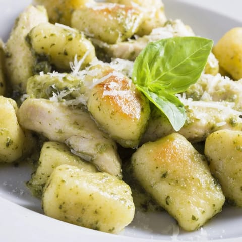 A close-up of Creamy Pesto Gnocchi with Chicken, highlighting juicy chicken pieces coated in rich sauce and garnished with fresh basil and grated Parmesan.