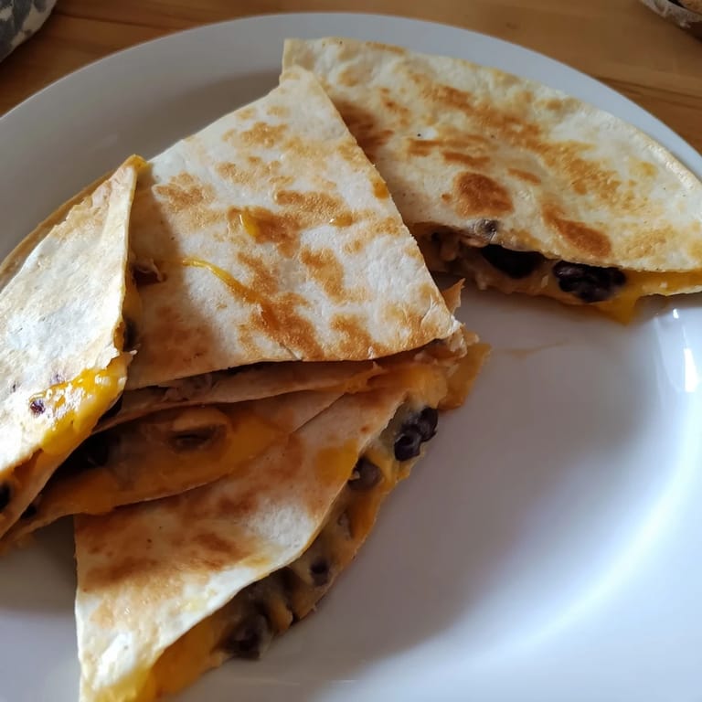 Warm, folded Bean & Cheese Quesadilla, perfectly browned and cut into wedges, ready to eat with toppings.