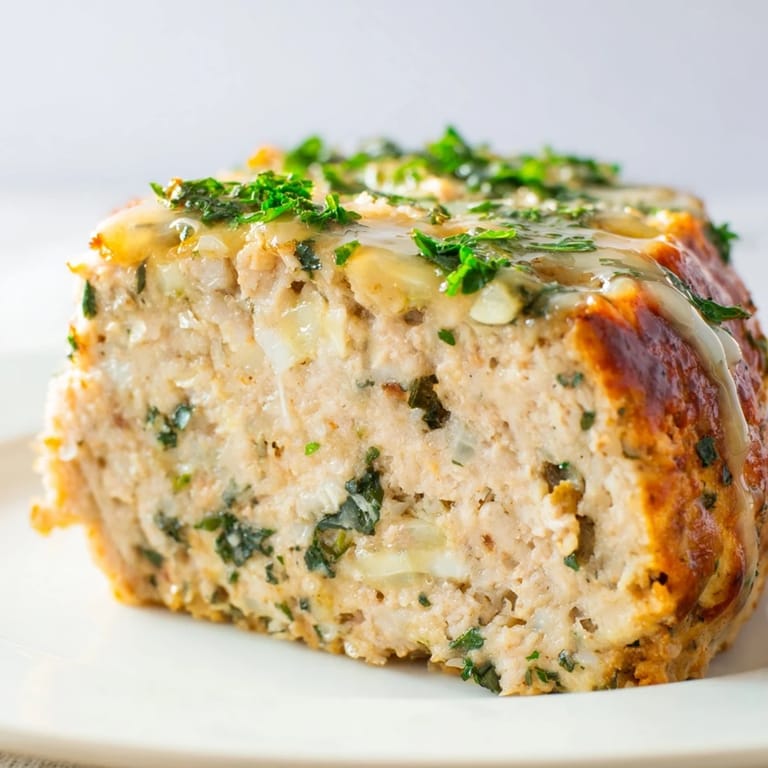 A close-up of savory Garlic Parmesan Chicken Meatloaf, showing its tender interior and herb garnish.